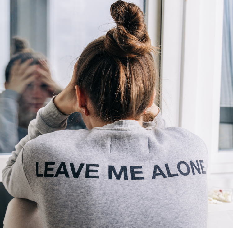 Ung kvinde, der sidder med ryggen til. På hendes trøje står der "leave me alone". Der er et pilleglas ved siden af hende
