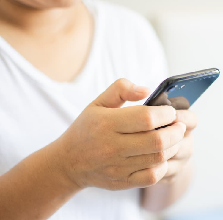 Yngre person, der holder en mobiltelefon i hænderne foran sig